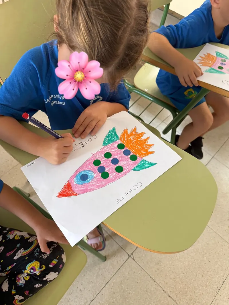 Dibujo de un cohete decorado con gomets sobre la mesa de un aula