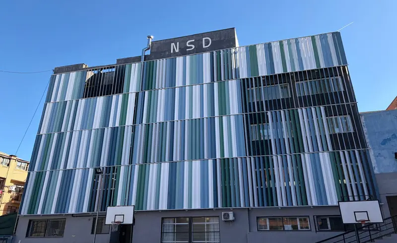 Fachada lateral del colegio con las lamas verdes y azules y las siglas NSD