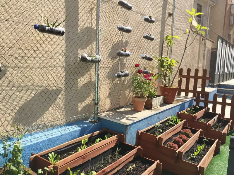Huerto del colegio, con jardineras de madera, macetas y botellas recicladas en la valla