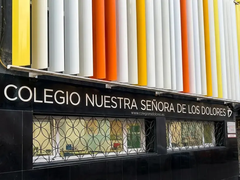 Rótulo del colegio en la fachada de la calle Tordo, bajo las lamas de colores